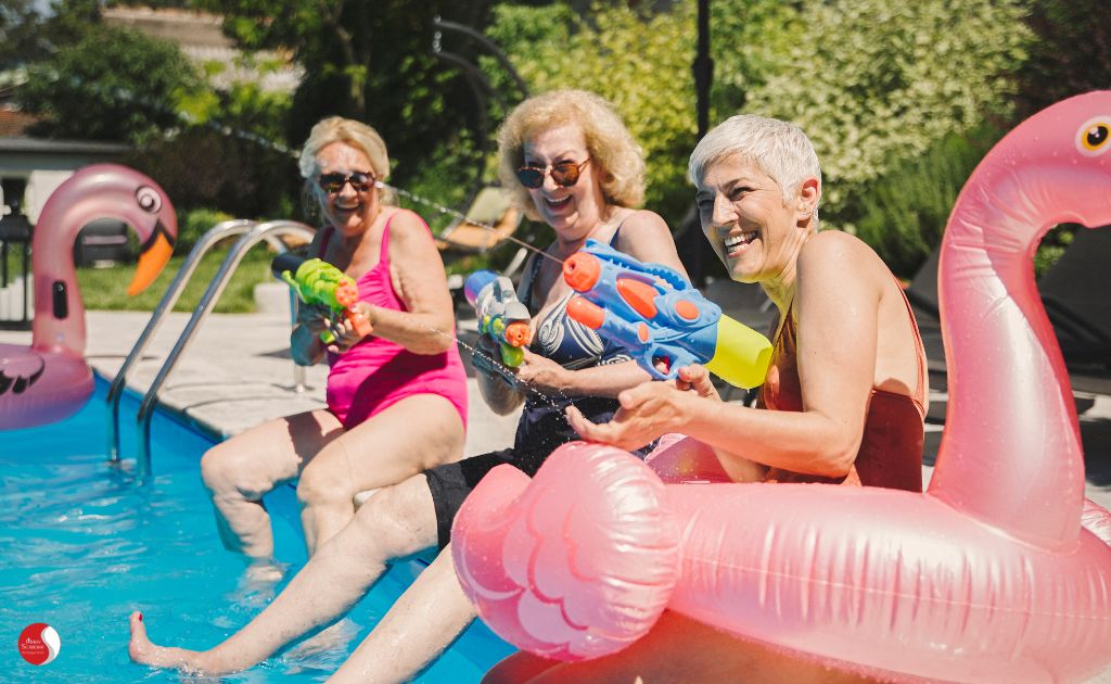 mulheres seniors brincando com jato de agua na beira da piscina exemplificando o cuidado si, envelhecimento e vida com qualidade