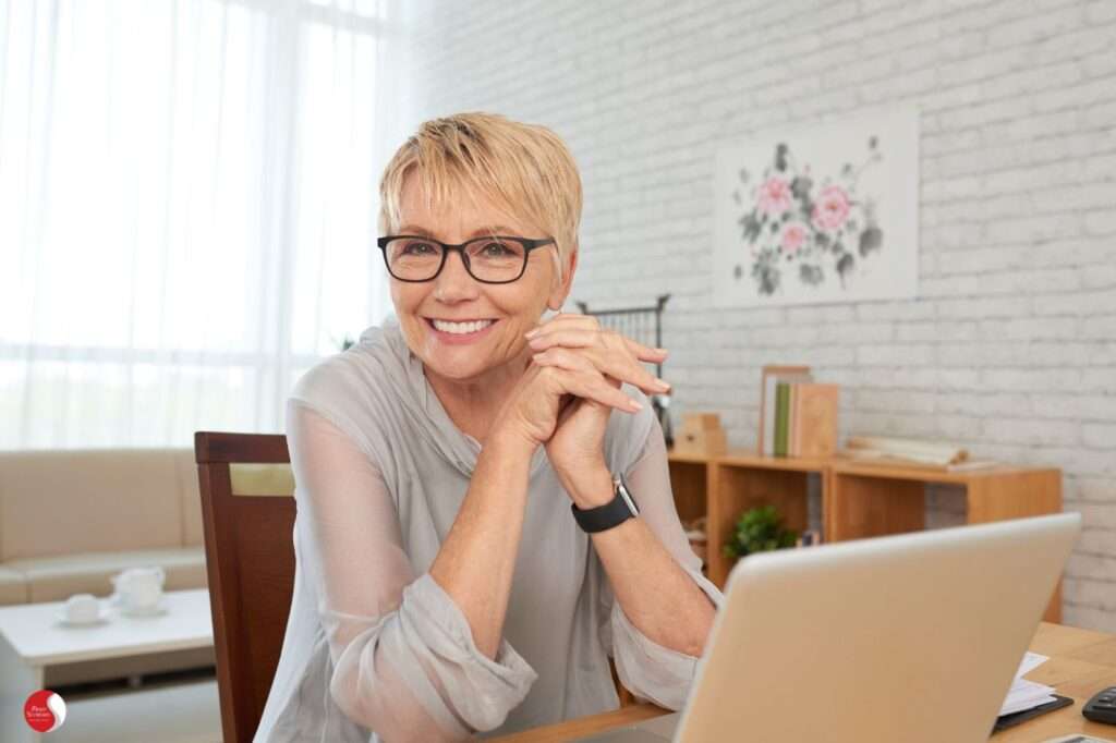 mulher idosa, sorridente trabalhando em frente ao computador. Simbolizando mudanças do envelhcer
