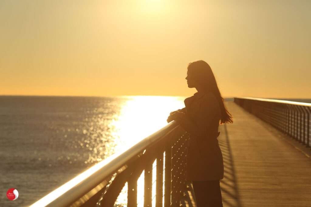 Mulher observando o mar ao pôr do sol, em momento de silêncio e introspecção — ilustrando como a terapia pode ajudar a mudar a forma de viver a própria vida, mesmo sem alterar os fatos externos.