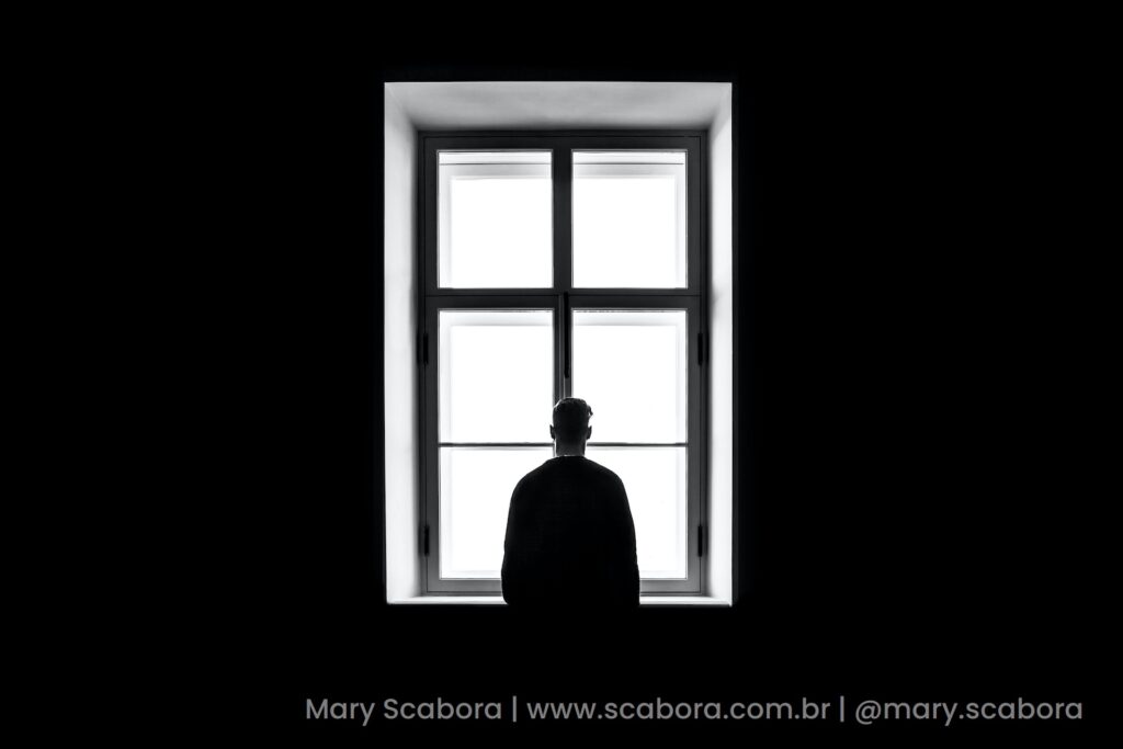 Como identificar a depressão ao seu redor imagem de homem na frente de uma janela com luz branca, dentro de um quarto escuro e sozinho