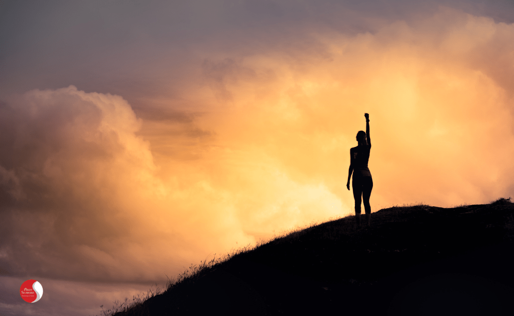 mulher em um morro no por do sol com o punho levantando simbolizando a eficacia do tratamento da ansiedde