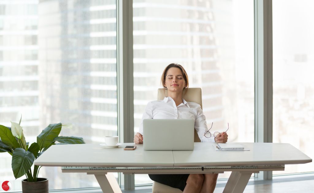 Mulher relaxando no escritório com os olhos fechados, ilustrando a prática de respiração profunda como técnica para controlar o estresse e promover o bem-estar no trabalho.