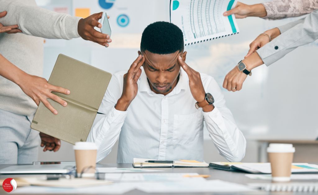 Homem pressiona as têmporas com expressão de estresse enquanto várias mãos ao redor apresentam tarefas e dispositivos, simbolizando a sobrecarga e pressão no ambiente de trabalho