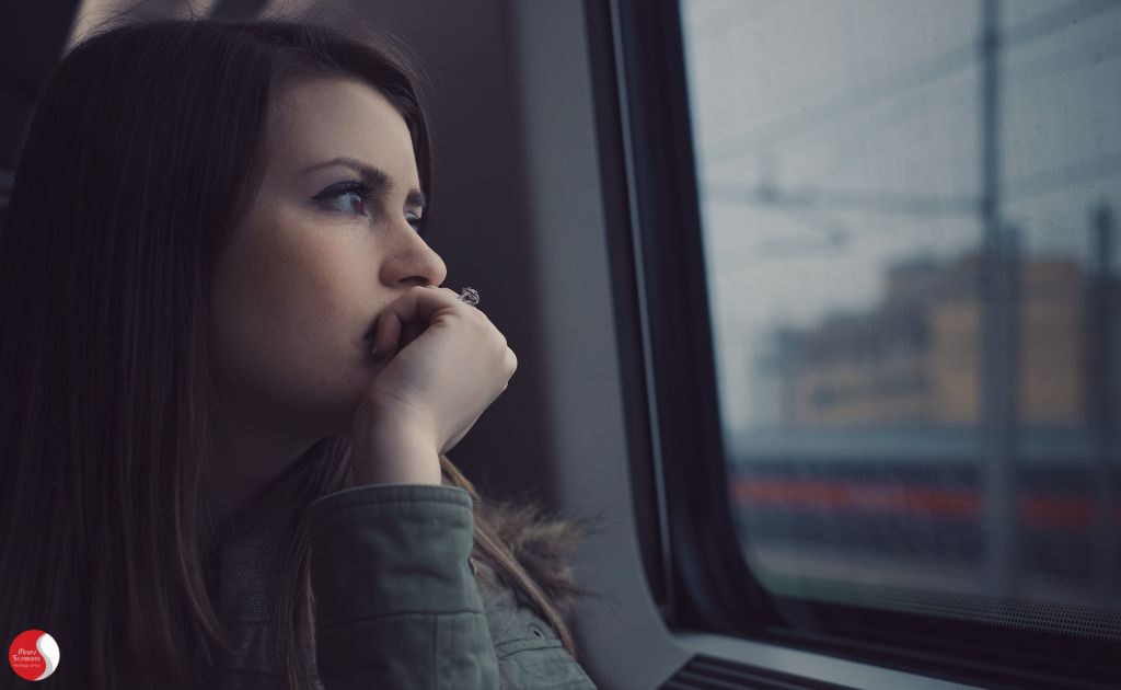 Mulher olhando pela janela com expressão contemplativa, simbolizando a desconexão emocional e o sentimento de vazio causado pelo Burnout.