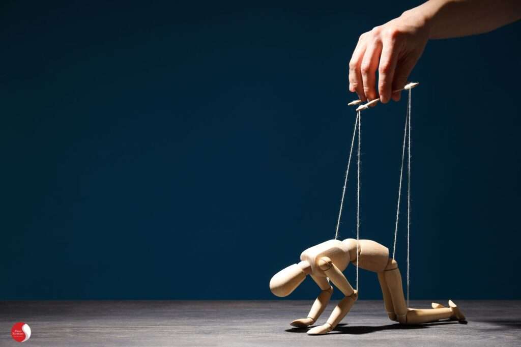 Boneco de madeira ajoelhado, sendo manipulado por fios, simbolizando o corpo exausto sob controle externo.