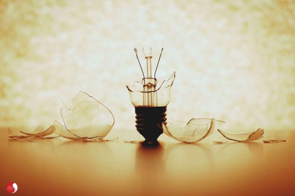 Lâmpada de filamento quebrada em fundo alaranjado, representando colapso energético causado pela síndrome de burnout.