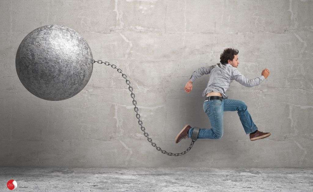 Homem corre com uma bola de ferro presa ao tornozelo por uma corrente, simbolizando um esforço constante apesar de um peso invisível que o retém.
