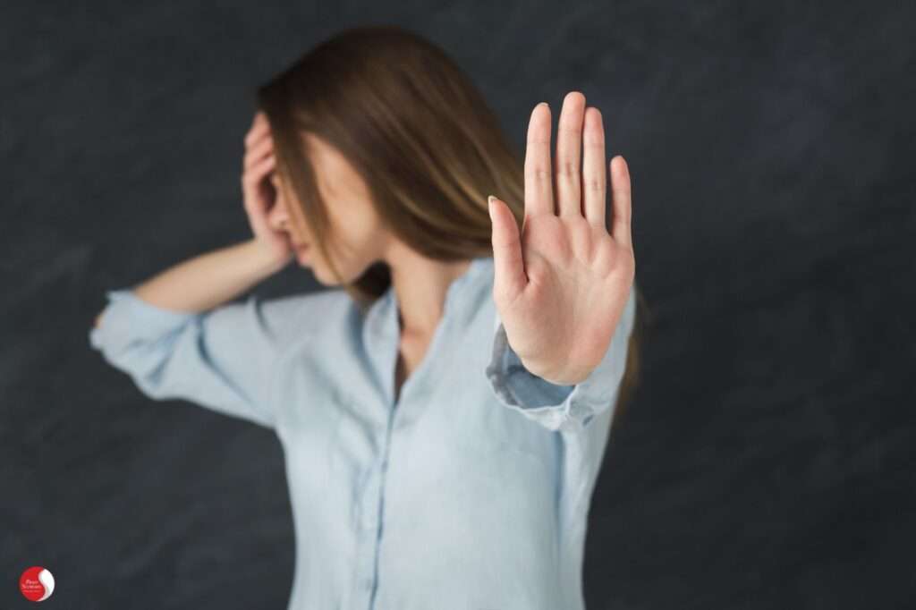 Mulher com expressão de desconforto emocional e mão estendida em gesto de recusa, simbolizando a negação da dor emocional.