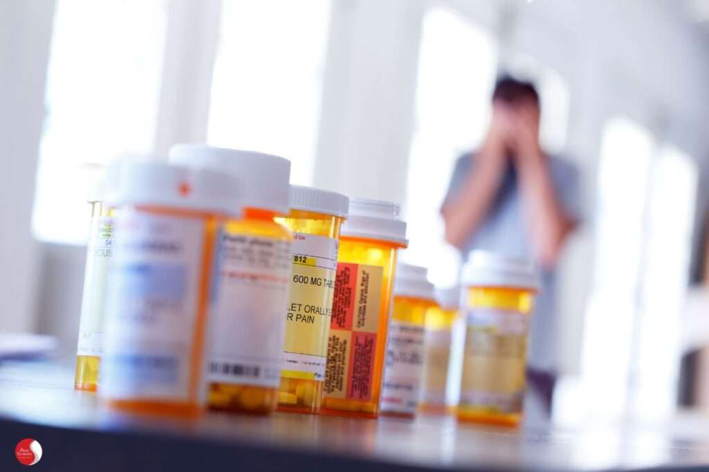 Frascos de remédio em destaque com pessoa angustiada ao fundo — simboliza a medicalização do sofrimento e dor emocional e a negação da escuta na prática médica.