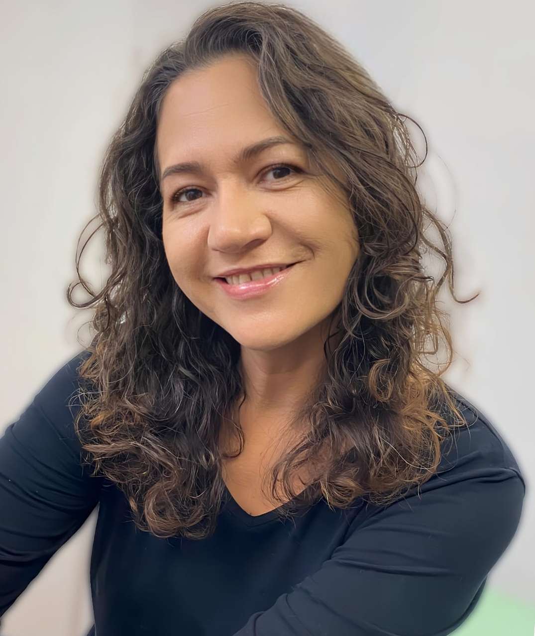 Psicóloga Mary Scabora sorrindo, com cabelos ondulados e blusa preta, em fundo neutro claro
