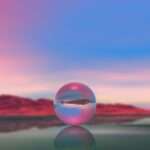 Esfera de vidro refletindo uma paisagem, com montanhas e barco ao fundo.