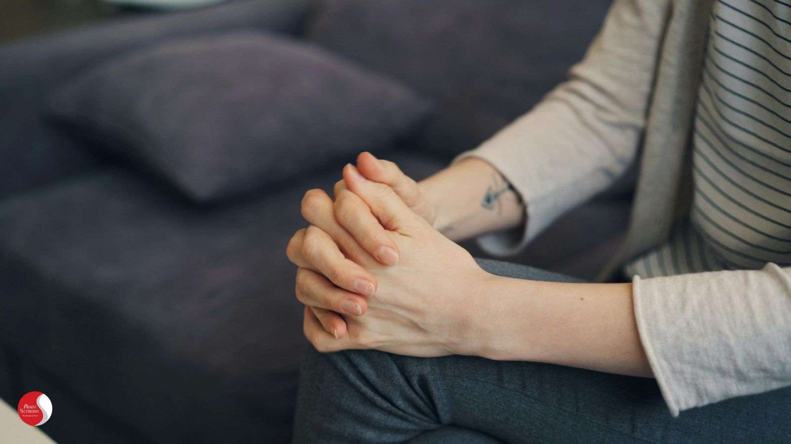 Pessoa sentada com as mãos entrelaçadas apoiadas sobre as pernas, imagem associada ao tratamento do transtorno do pânico.