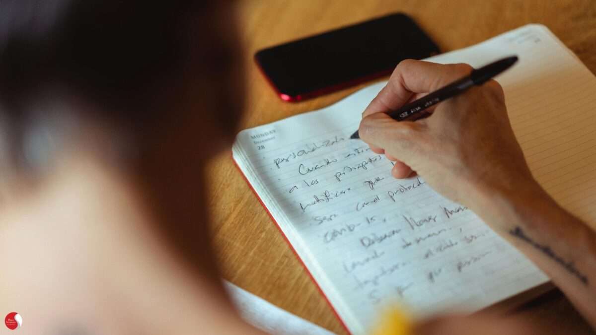 Mulher escrevendo à mão em caderno aberto, representando o processo de elaboração emocional na psicoterapia