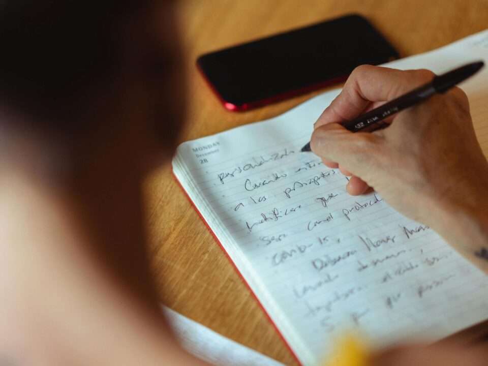 Mulher escrevendo à mão em caderno aberto, representando o processo de elaboração emocional na psicoterapia